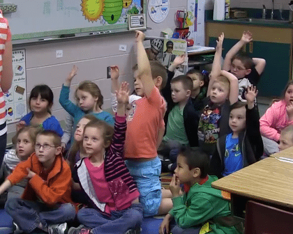 Children in a kindergarten class eagerly raising their hands ready to ask questions.