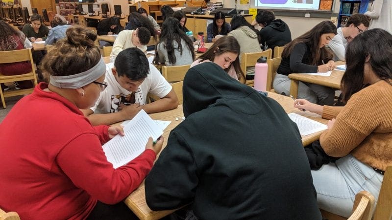 students peer editing essays at tables in the school library